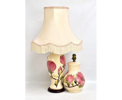 MOORCROFT; two 'Magnolia' pattern tubeline decorated lamp bases on cream grounds, the larger on wooden base, height excluding