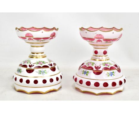 A pair of late 19th century Bohemian overlaid cranberry tinted and painted enamel decorated low table lustres, the upper band