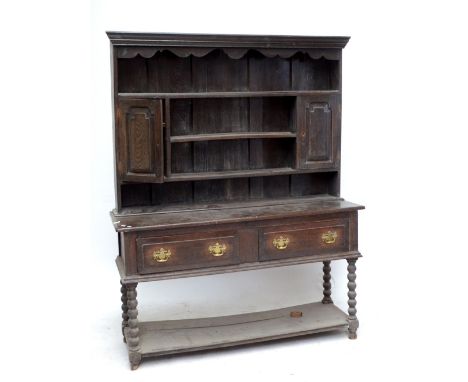 An oak dresser with boarded plate rack set with twin cupboard doors above a base of two drawers raised on bobbin turned legs 