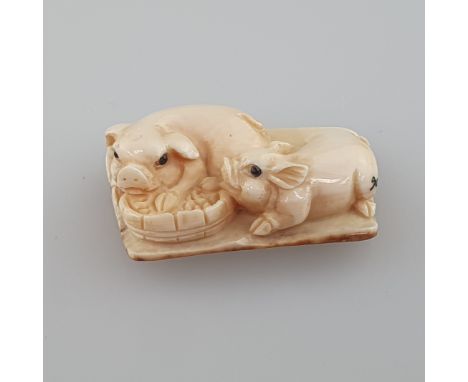 Netsuke - Zwei Schweinchen am Trog, Mammutbein, geschnitzt, dunkel eingelegte Augen, signiert, Himotoshi auf der Unterseite, 