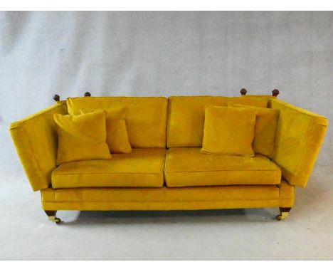 A contemporary Knole sofa in gold upholstery raised on squat square tapering supports on brass cup casters. H.93xW.229xD.104c