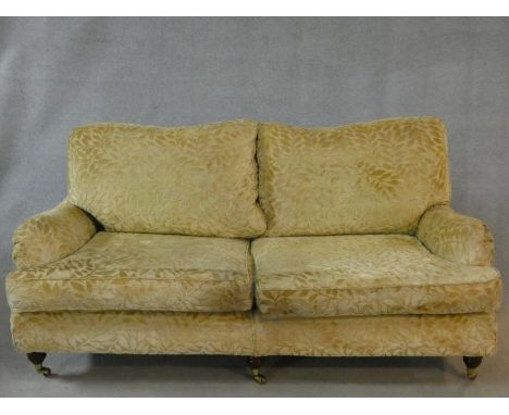 A two seater Howard style sofa in cut floral upholstery on triple squat turned tapering supports terminating in brass cup cas