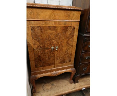 Mid 20th Century figured walnut side cabinet, the carved moulded top above a pair of panel doors on carved cabriole claw and 