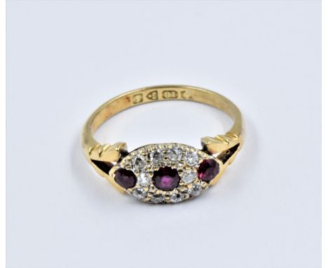 18ct Gold ruby and diamond dress ring, the oval head with three small rubies surrounded by ten small diamonds and flanked by 