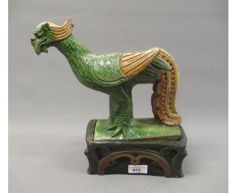 Chinese brown and green glazed pottery roof ridge tile in the form of a standing exotic bird on a carved and painted wooden b