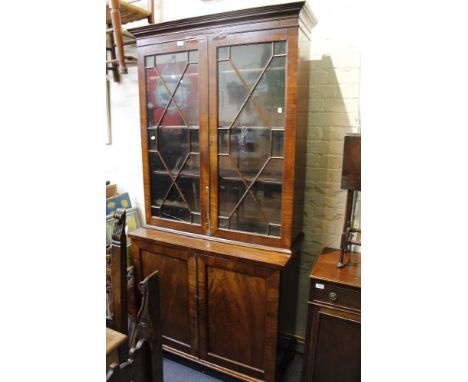 A 19TH CENTURY MAHOGANY BOOKCASE CABINET with twin astragal glazed doors above twin panelled doors below, raised on bracket f