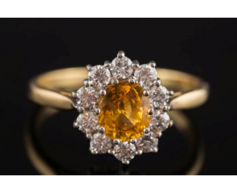 An 18ct gold, yellow sapphire and diamond oval cluster ring: the central, yellow sapphire 7mm long x 5.6mm wide within a surr