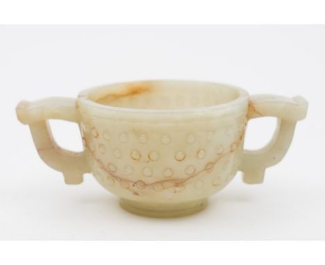 A Chinese jade two-handled cup: of archaic form with flattened loop handles, the body carved with four rows of studs, the sto