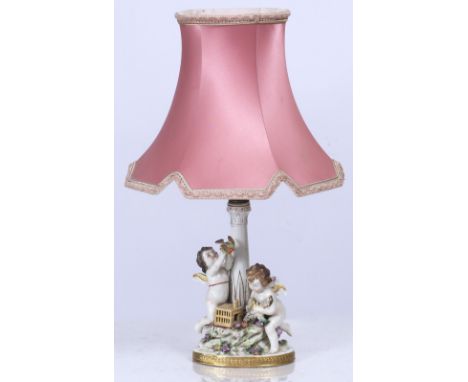 A NAPLES PORCELAIN TABLE LAMP depicting two cherubs releasing birds beside a column, the base 14cm wide x 29cm high including