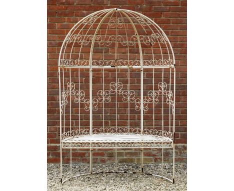 A WHITE PAINTED METAL ROSE ARBOUR SEAT of demi lune form with scrolling wire work supports and a cushion 123cm wide x 60cm de