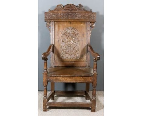 A 17th Century Panelled Oak "Wainscot" Armchair, the high back with shaped cresting carved with leaf ornament, the rear panel