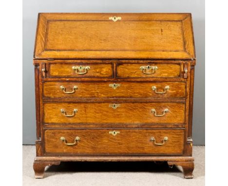 A George III Oak and Mahogany Banded Bureau, the slope enclosing central cupboard, pigeon holes and eight small drawers, fitt