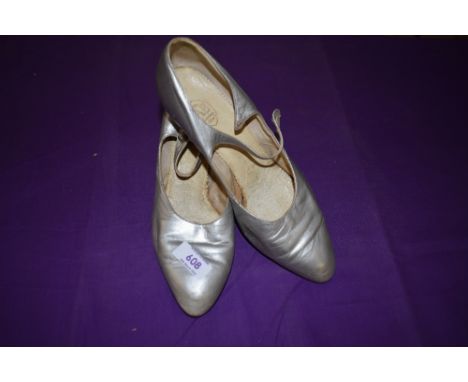 A pair of 1930s silver shoes having leather soles and button fastening to sides, one button missing.