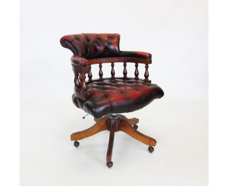 An oxblood red leather revolving desk chair, late 20th century, with button back seat and padded arms on turned spindles, rai