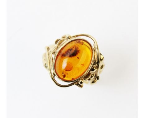 An amber set 9ct gold ring, comprising a central oval amber cabochon, measuring 16mm x 11mm, bezel set to stylised foliate sh