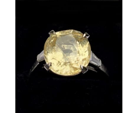 A yellow sapphire and diamond ring, the central cushion mixed cut sapphire claw set with a baguette cut diamond to each shoul