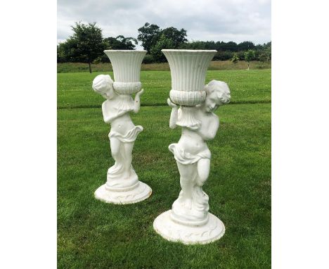 A pair of cast iron figural jardinieres, white painted, each modelled as a scantily clad putti supporting a campana type plan