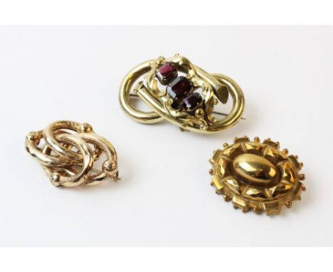 A Victorian garnet set love knot brooch, comprising three step cut garnets claw set in yellow metal to a scrolling border sur