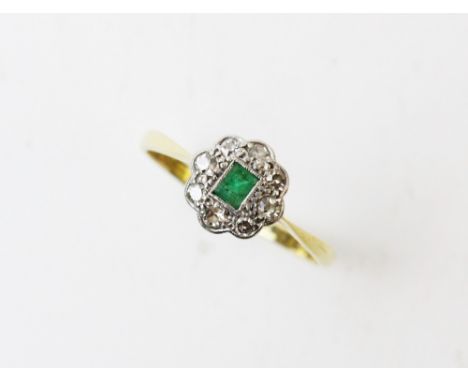 An early 20th century emerald and diamond ring, comprising a central rectangular step cut emerald with a cluster surround of 