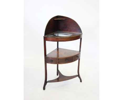 A George III mahogany corner washstand, the upper bow front shelf with three bowl apertures, above a second shelf with a sing