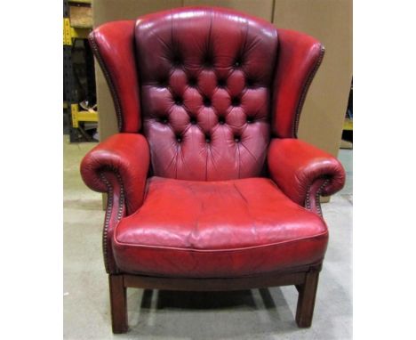 A contemporary Georgian style red leather upholstered wing armchair with button back and loose squab seat cushion raised on s