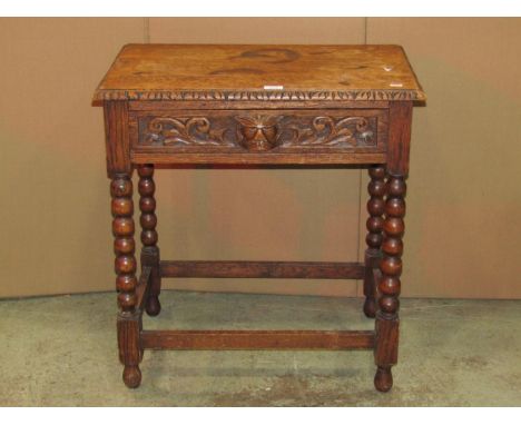 A 1920s oak side table fitted with a frieze drawer with carved green man mask cup handle and scrolling acanthus detail raised