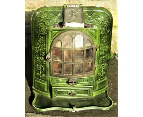 A French cast iron and green enamel stove enclosed by a bow fronted arched panelled door within a decorative foliate surround