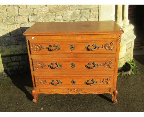A medium to light oak commode of three long drawers with carved foliate detail and fixed cast scrolling acanthus handles over