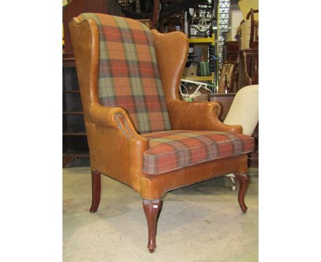 A substantial Georgian style wing armchair with shaped outline and wide generous seat partially upholstered in light tan leat