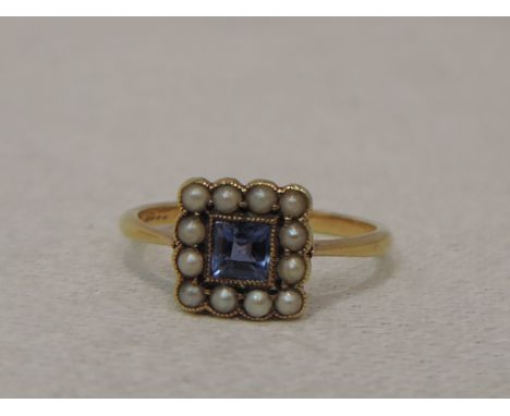 A lady's dress ring having an emerald cut powder blue sapphire within a seed pearl border on a yellow metal loop stamped 18ct