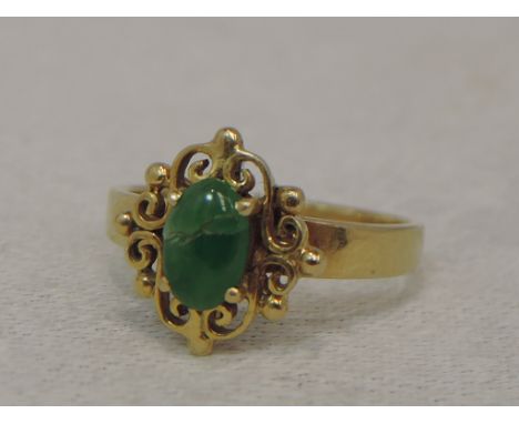 A lady's dress ring having a green cabouchon stone in a claw set decorative mount on a yellow metal loop stamped 585,  size N