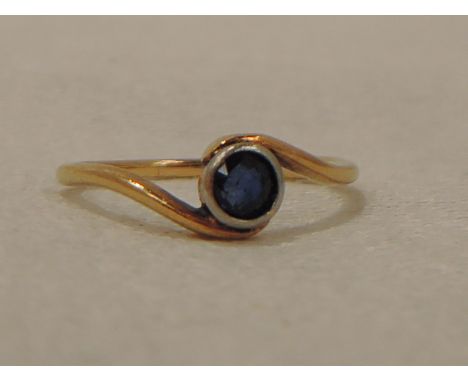 A lady's dress ring having a sapphire solitaire in a collared mount to cross over shoulders on a yellow metal loop stamped 18