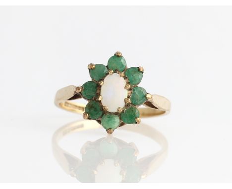 A 9ct yellow gold opal and emerald ring, claw set with a central oval opal cabochon measuring approx. 4x6mm, surrounded by a 