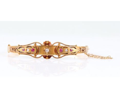 An Edwardian 15ct yellow gold diamond and ruby hinged bangle, set with a central old European cut diamond, measuring approx. 