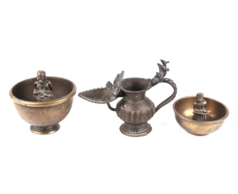 Two Indian brass drunkard cups with central figures, the largest 12cms diameter; together with an oil lamp, 13cms high (3).