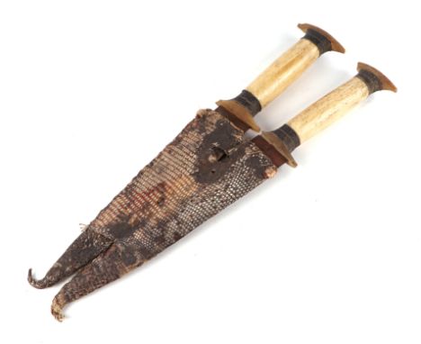 A pair of African tribal daggers, having matching bone and horn hilts, twin double edged blades, and snake skin double scabba