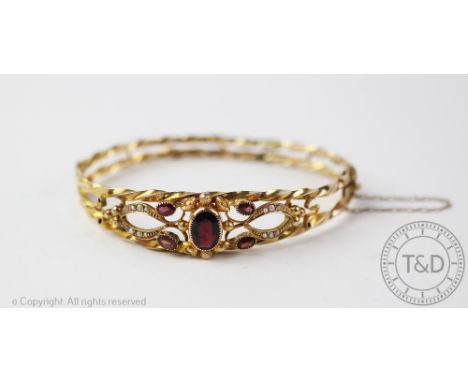 A 9ct gold garnet and seed pearl set hinged bangle, designed as a central garnet within a split seed pearl set surround and r