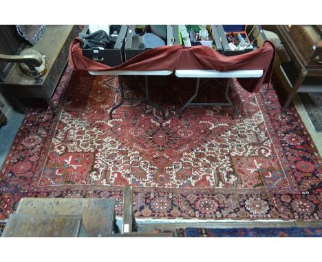 A Persian Heriz carpet, the stylised geometric and floral designs on red ground centred by a large medallion within a navy bo