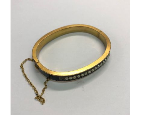 A Victorian mourning half hinged yellow metal and black enamel bangle, set with fifteen half pearls, safety chain attached