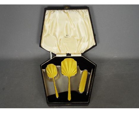 A cased four piece silver and enamel dressing table set comprising hand mirror, hair brush, clothes brush and silver mounted 