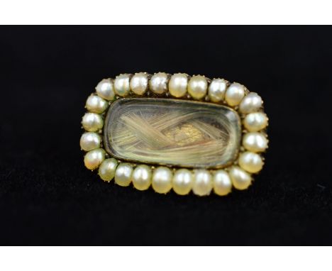 A LATE GEORGIAN GOLD MEMORIAL BROOCH of rectangular outline, the central glass panel enclosing a lock of hair, to the split p