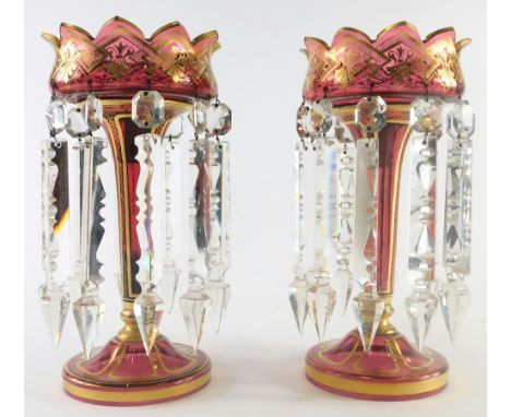 A pair of late 19thC Bohemian ruby glass lustres, with gilt highlights, floral tops, inverted stems and circular feet, with p