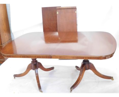 A mahogany two pillar dining table in Regency style, the rectangular top with a cross banded border, each support with a turn