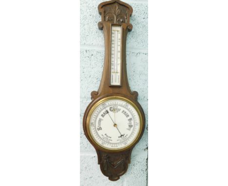 An early 20thC oak cased thermometer and barometer, with 19cm diameter dial, heavily carved case set with fleur de lys and sc