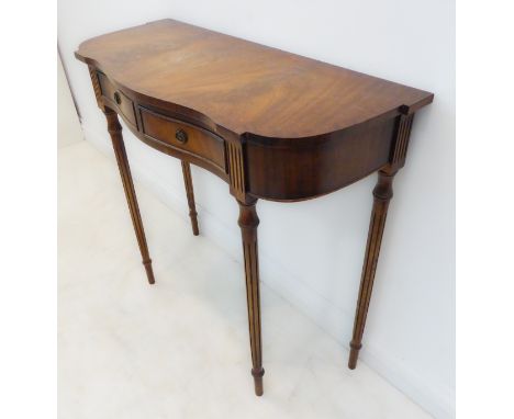 A reproduction serpentine-fronted mahogany and crossbanded two-drawer console table raised on finely turned tapering and flut