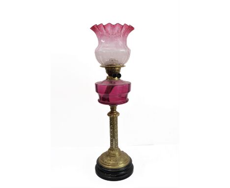 A 19th century brass-mounted oil lamp with cranberry glass reservoir and crimped shade: foliate decoration to the stem and wi