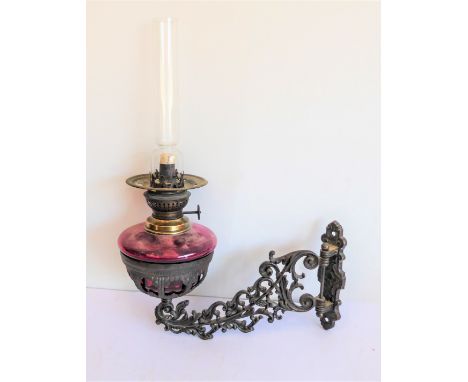 A 19th century wall-mounting oil lamp: circular cranberry glass reservoir locating into a pierced metal support (approx. 29 c