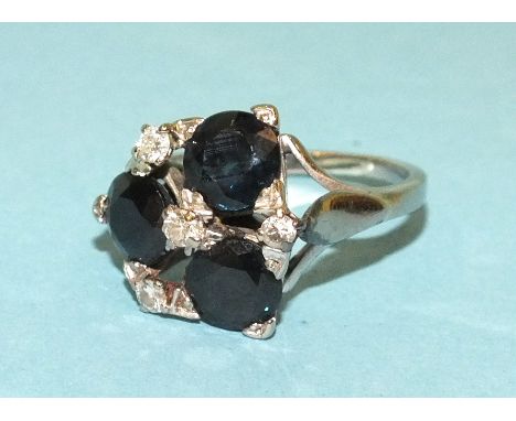 A sapphire and diamond ring claw-set a cluster of three round-cut sapphires, with diamond points between, in 18ct white gold 