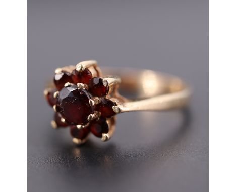 A cased vintage daisy set garnet ring, having a central 5 mm brilliant stone set above an annulus of eight 2.5 mm garnets, be