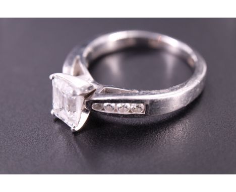 A contemporary emerald cut diamond solitaire ring, having a one carat diamond in a four prong Tiffany style basket setting, s